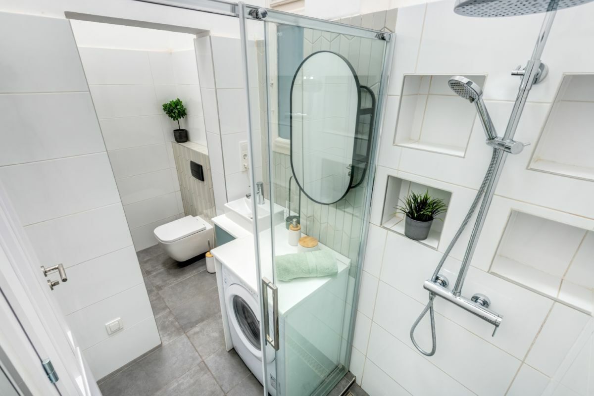 Egységes fehér falburkolatok a fürdőben praktikus tárolópolccal kombinált tükörrel