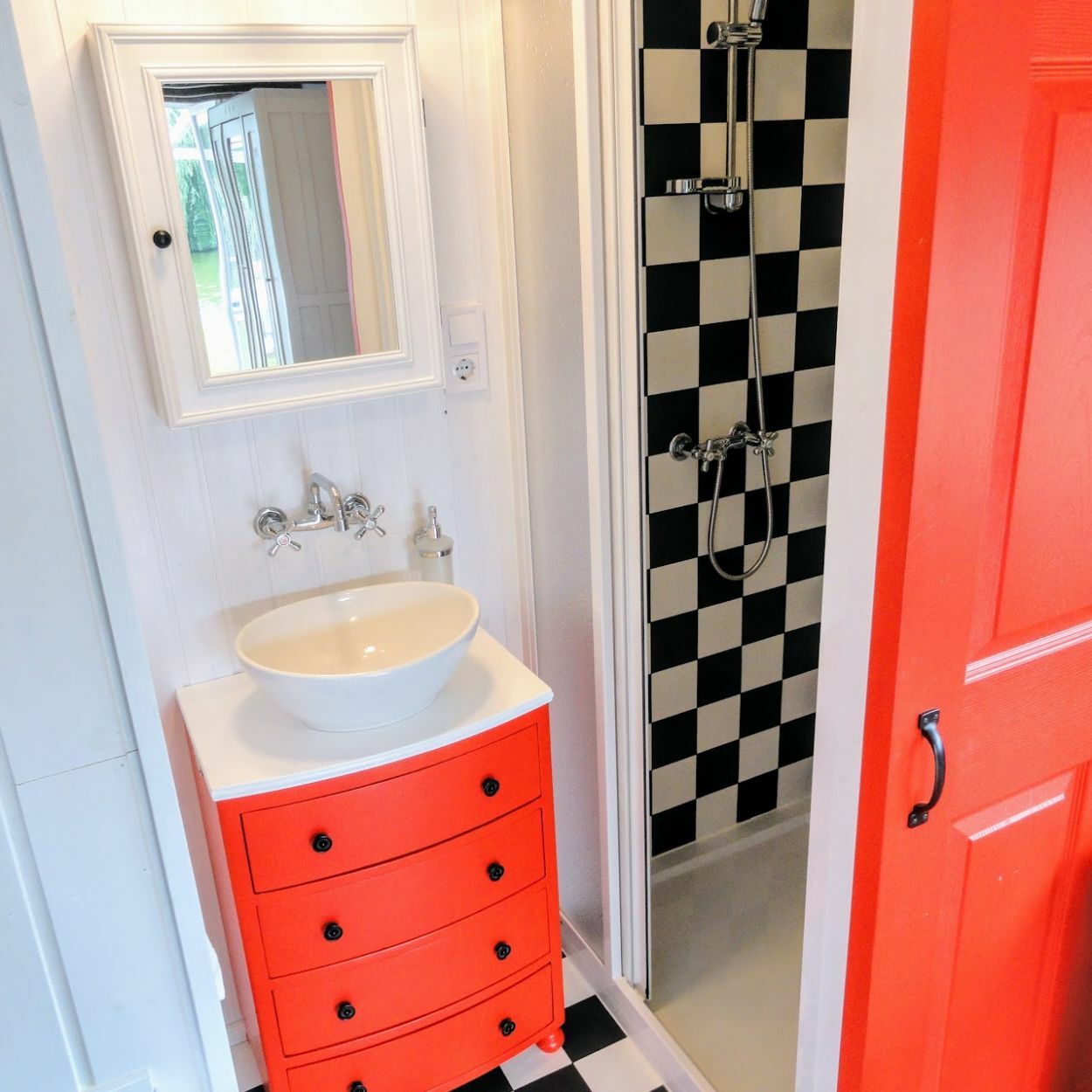 Élénkpiros fürdőszobai szekrény és fekete-fehér kockás burkolat a zuhanyzóban